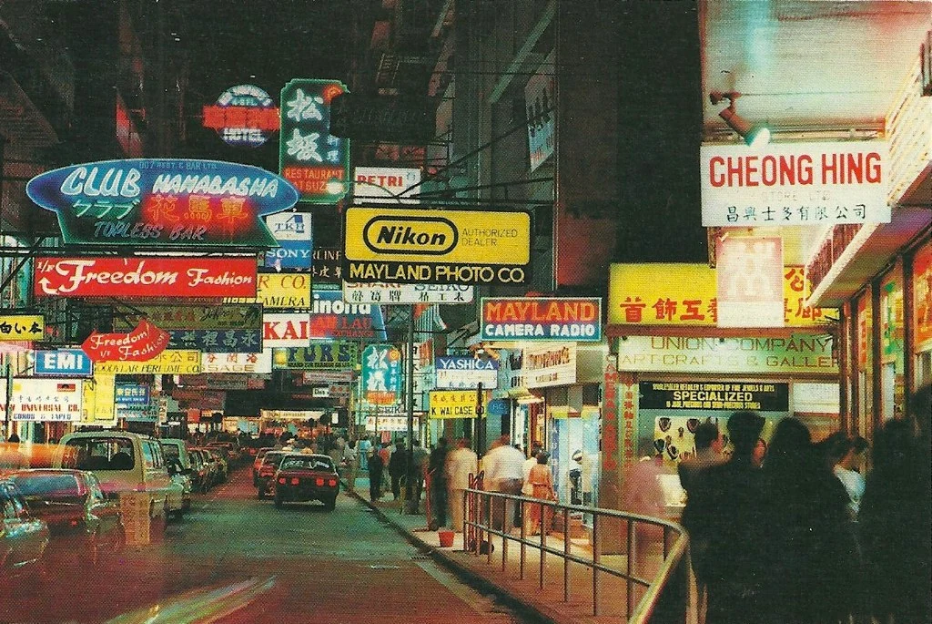 舊日尖沙咀街頭,相機舖同夜總會招牌伸出街外,的士同人群喺下面經過